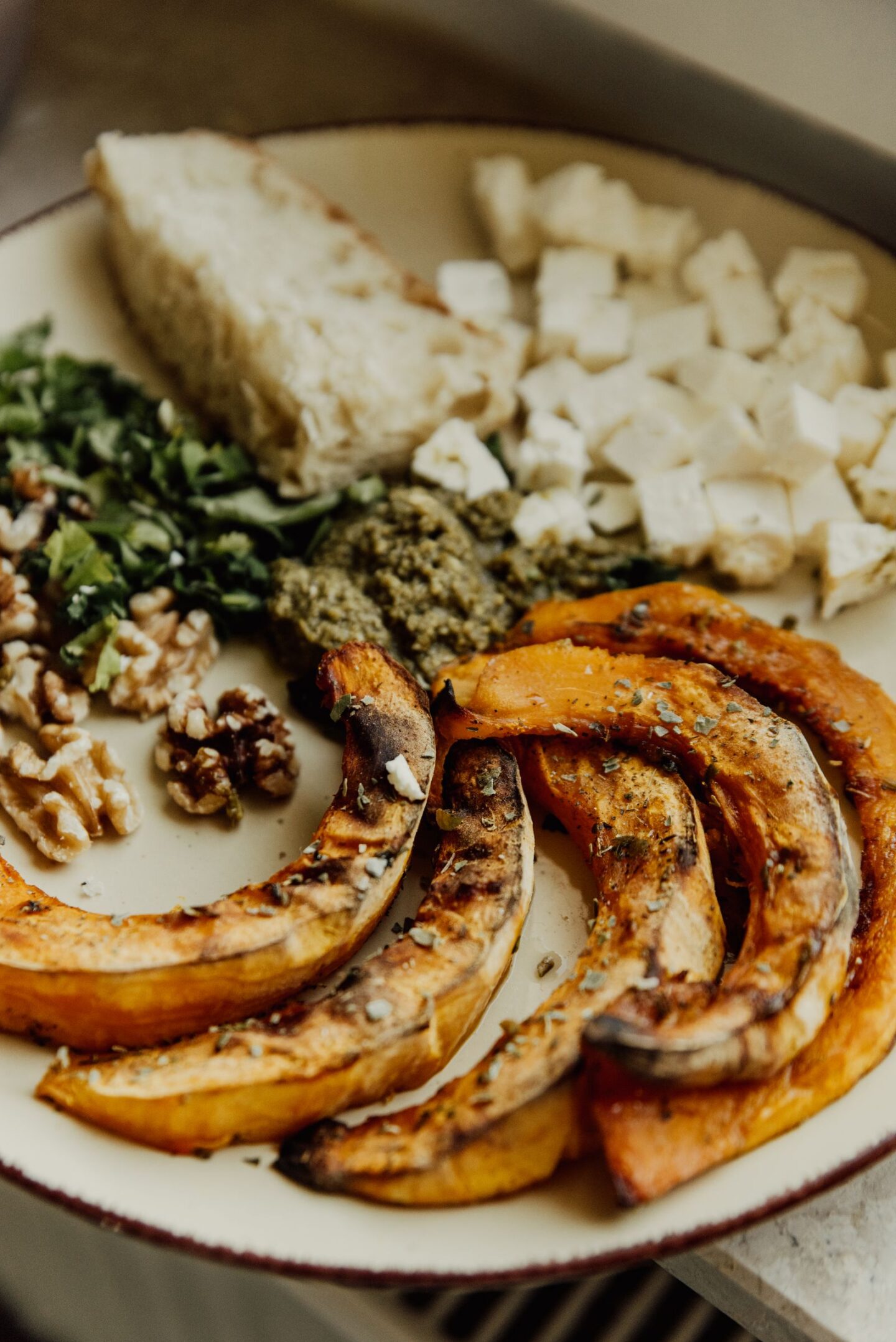 Bord met geroosterde plakken pompoen, verse kruiden, noten, feta en brood